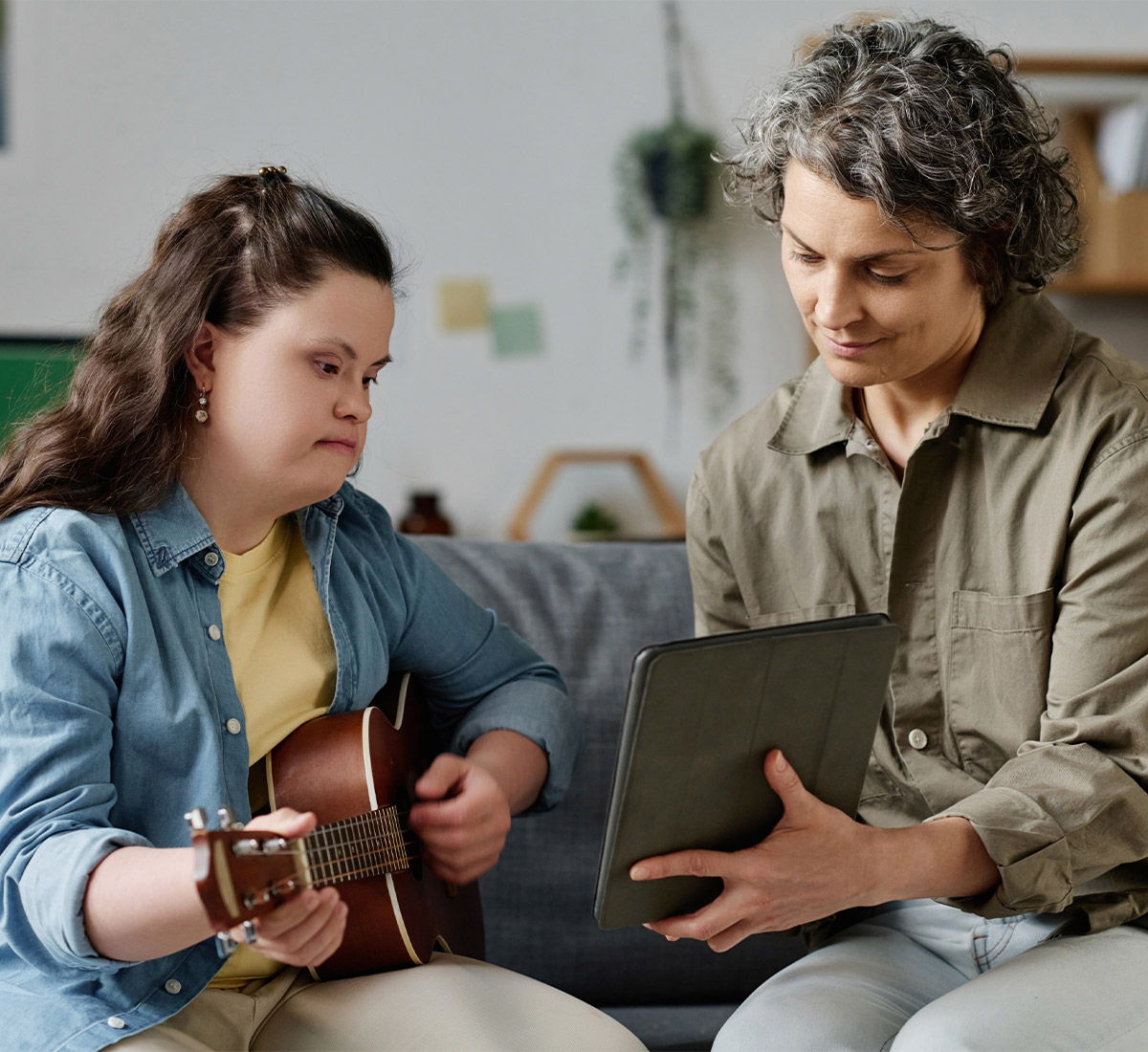 Junge Frau mit Down-Syndrom und Assistenzkraft lernen Gitarre spielen