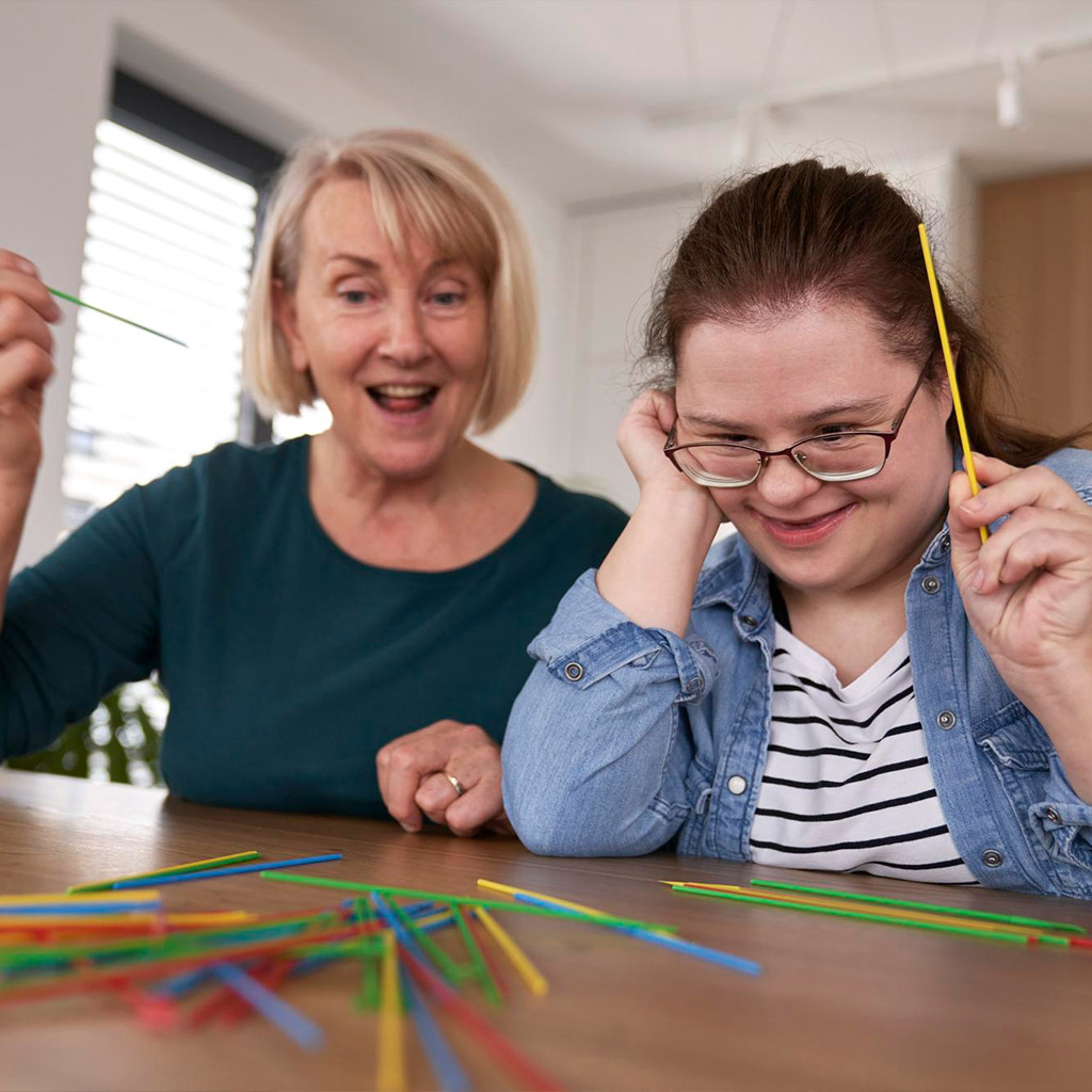 Frau mit Down-Syndrom spielt gemeinsam mit einer Assistenzkraft.